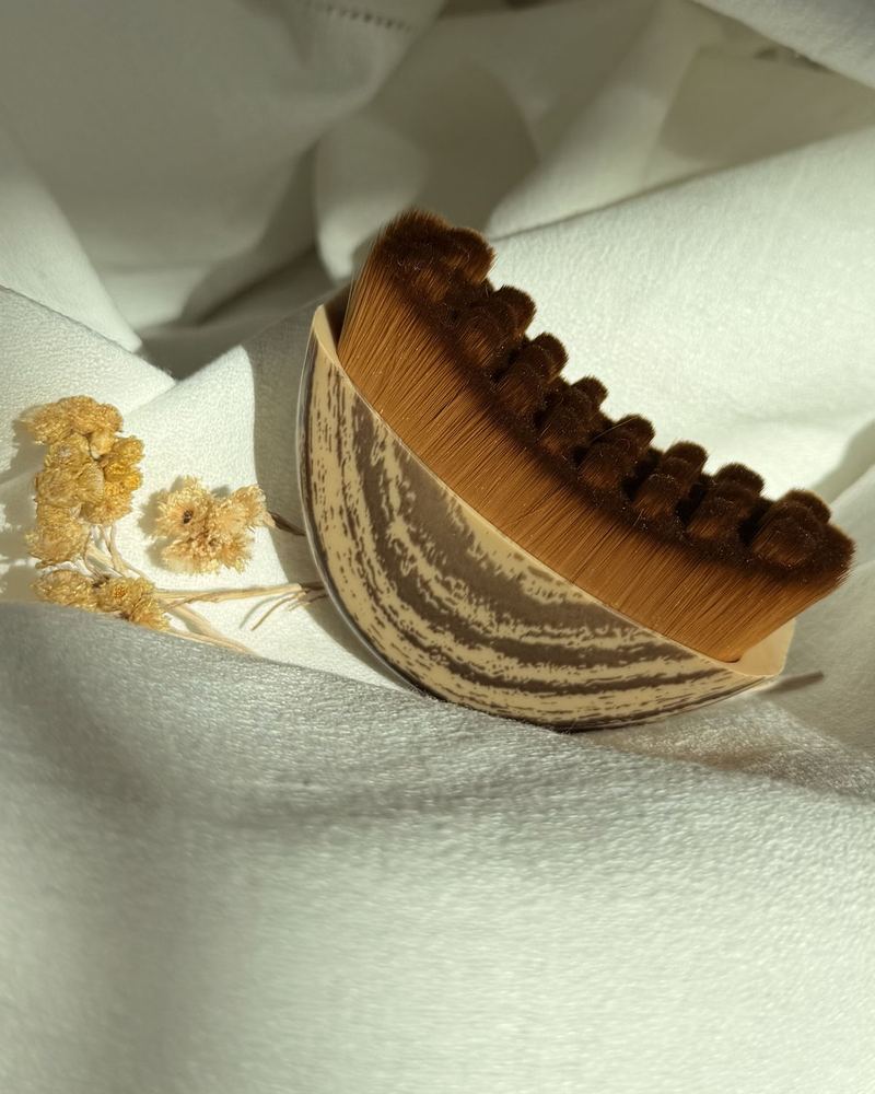 Brosse visage en demi-lune posée sur un linge clair